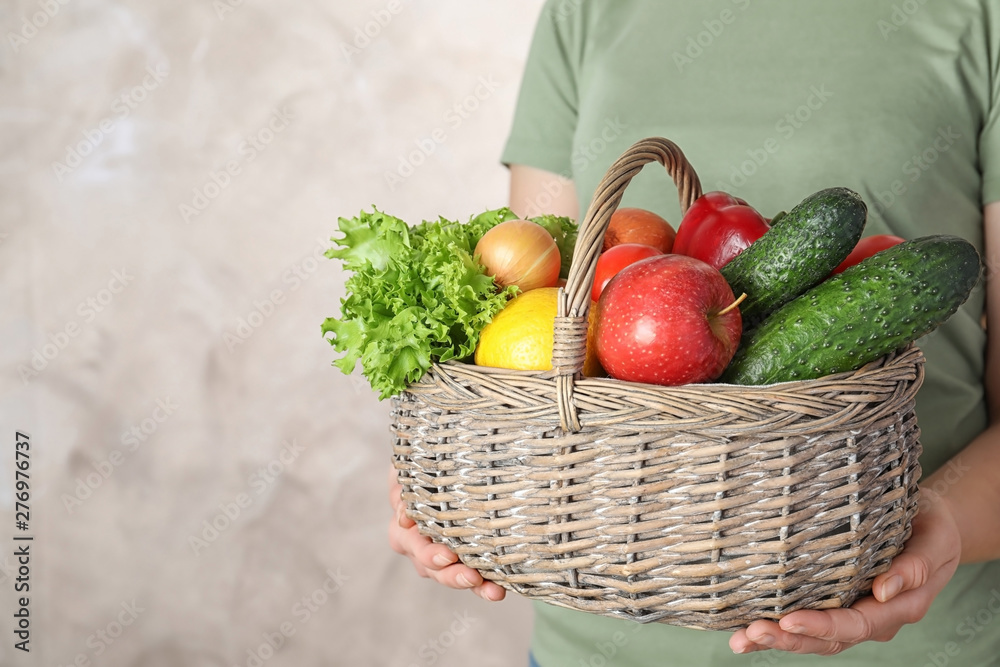 Fototapeta premium Woman holding wicker basket with ripe fruits and vegetables on color background, closeup. Space for text