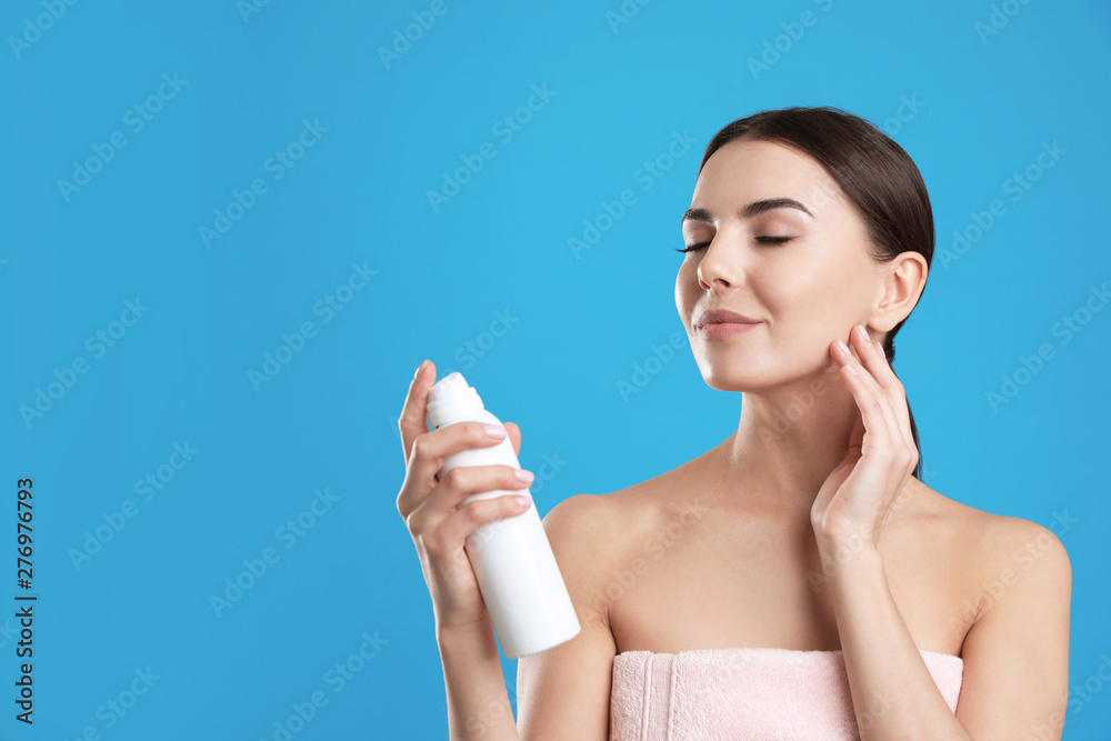 Young woman applying thermal water on face against color background, space for text. Cosmetic product Young woman applying thermal water on face against color background, space for text. Cosmetic product