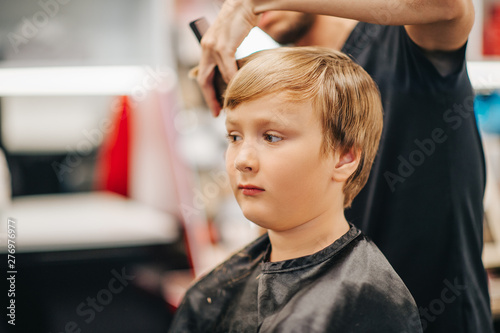 Young kid boy getting new haircut in barber shop