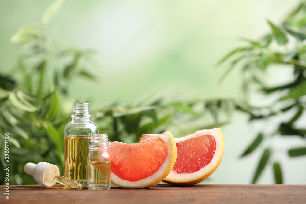 Bottles of essential oil and grapefruit slices on table against blurred background. Space for text Bottles of essential oil and grapefruit slices on table against blurred background. Space for text
