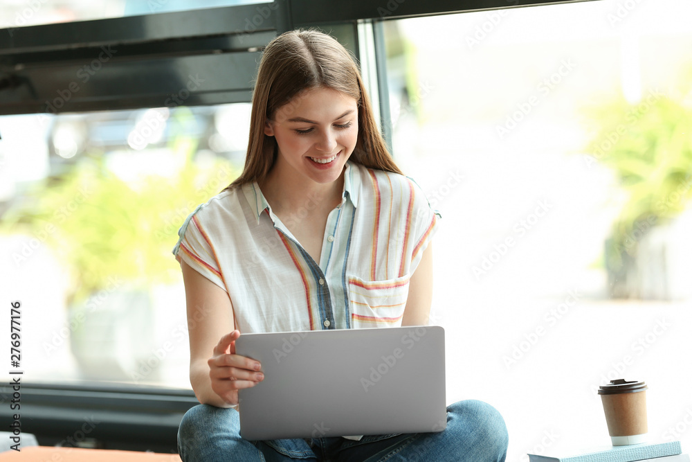 Young woman working on laptop near window in library Young woman working on laptop near window in library
