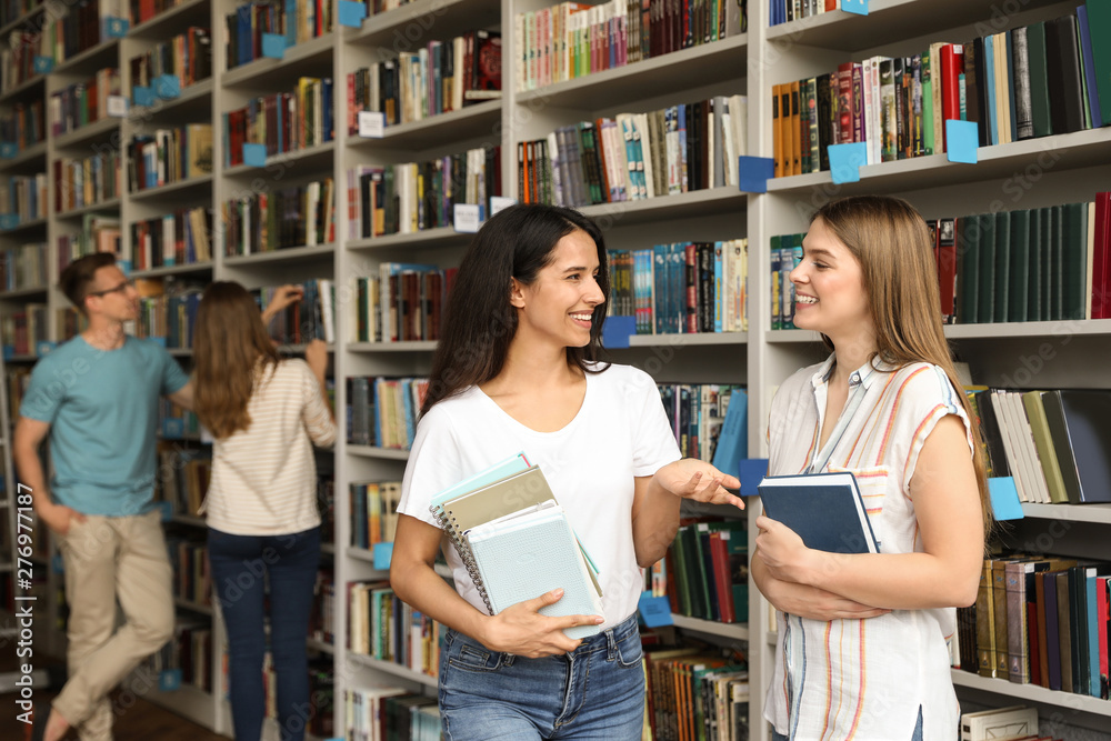Young people standing near bookshelves in library Young people standing near bookshelves in library
