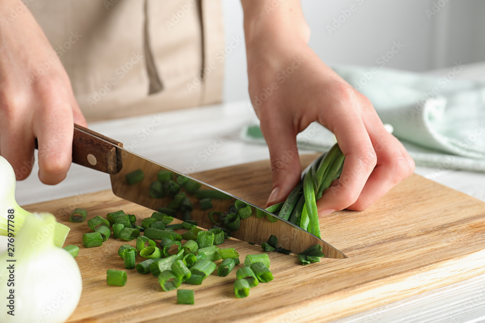 Woman cutting fresh green onion on wooden board at table, closeup Woman cutting fresh green onion on wooden board at table, closeup