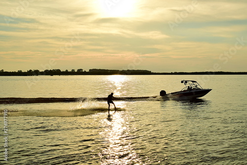 Skiing on a slalom ski. Wakeboarding. Little boat rolls the man on the mono ski. The river in the sunset.