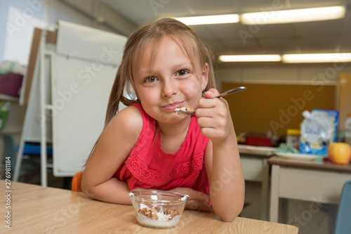 Elementary School Girl Having Granola And Yogurt Snack In Classroom At School