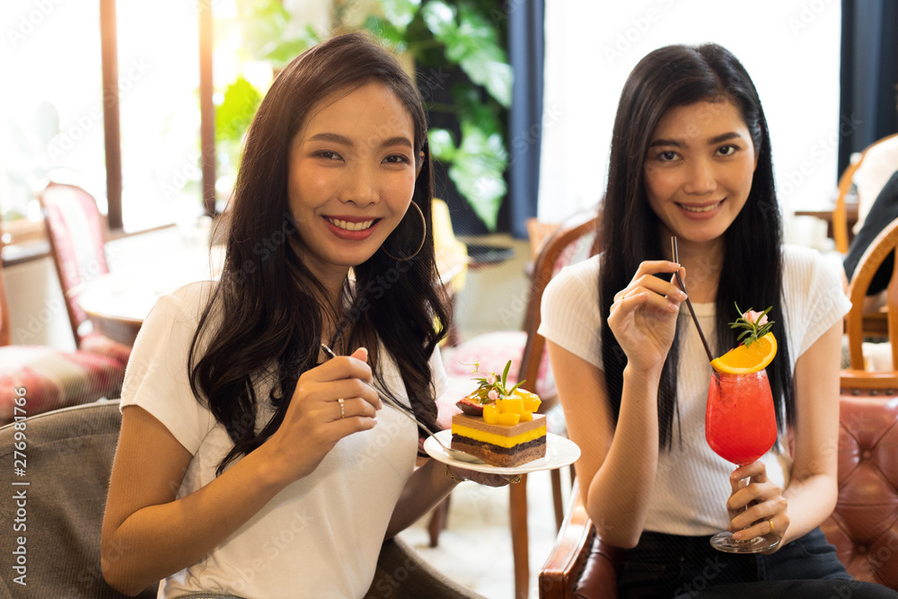 Two Asian Sisters take photo and taste delicious sweet Cake and Fruit Juice, Best friends smile together for beautiful design cake and smoothies refreshment in boutique restaurant cafe during travel Two Asian Sisters take photo and taste delicious sweet Cake and Fruit Juice, Best friends smile together for beautiful design cake and smoothies refreshment in boutique restaurant cafe during travel