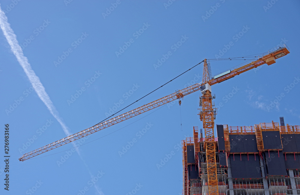View of a yellow skyscraper construction crane under blue sky with a jet trail 