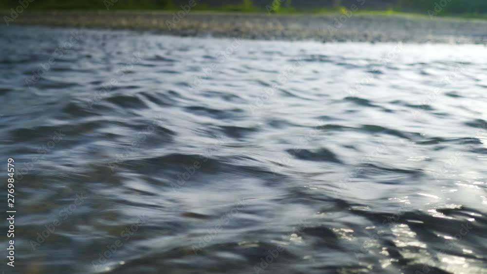 Close shot of a big river running fast past the camera, still shot. Sandy riverbank in the background. Sunny day.