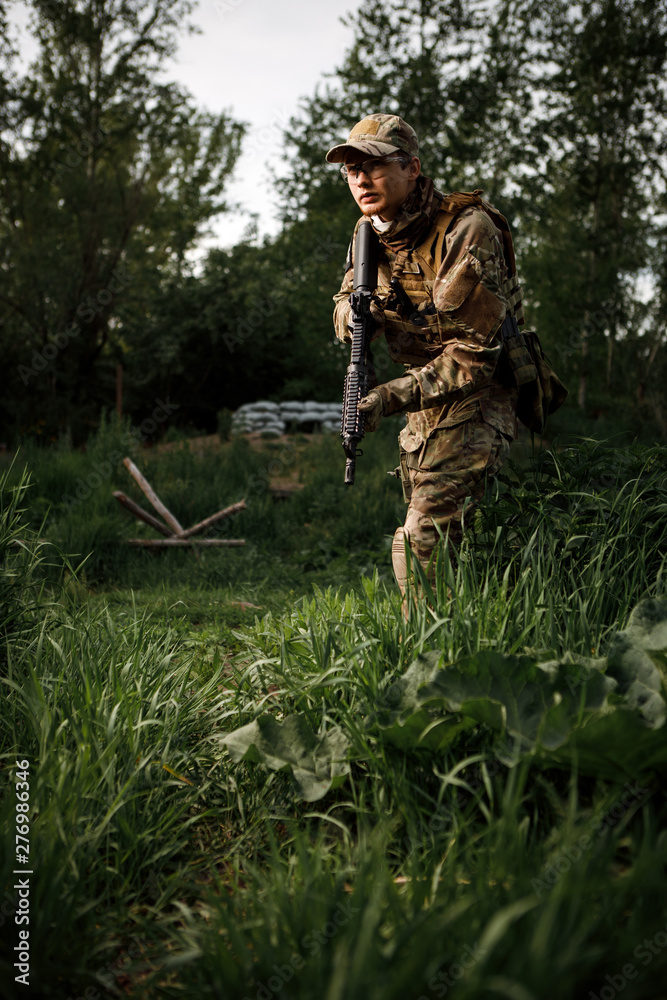 Airsoft soldier in full ammunition with rifle playing strikeball in outdoor in grass