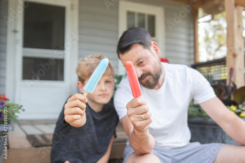 Father and son holding up ice pops on a porch in summer