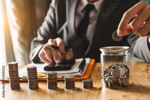 businessman holding coins putting in glass with using smartphone and calculator to calculate concept saving money for finance accounting