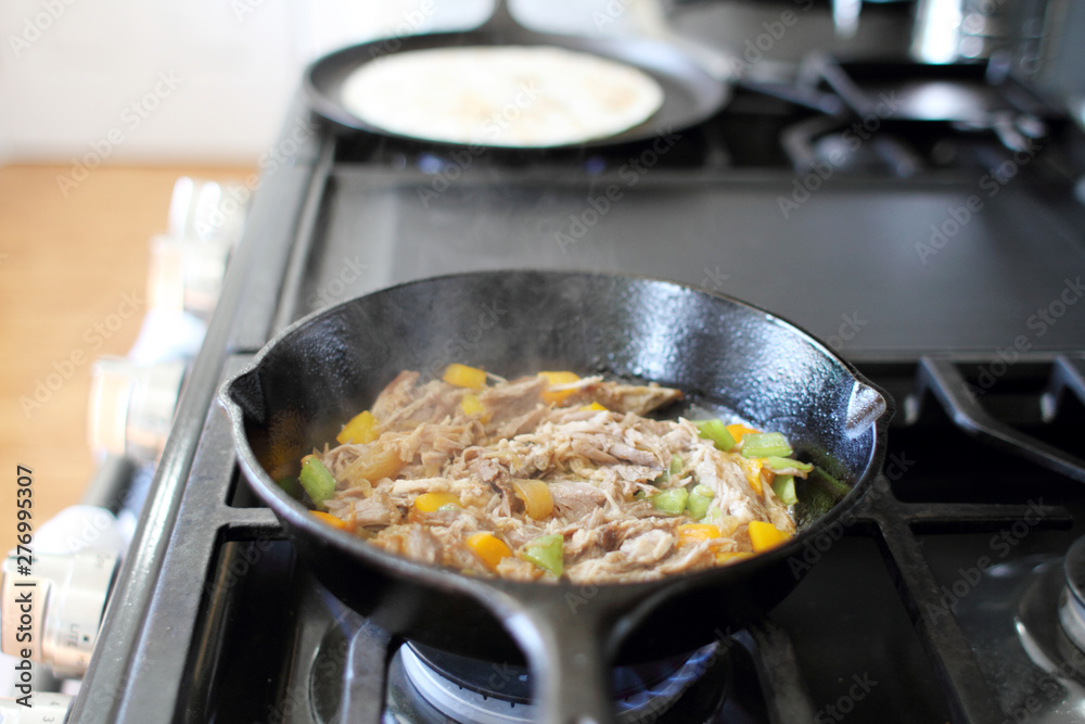 Mexican style pulled pork, known as carnitas, cooking in a cast iron skillet with a flour tortilla on a camal skillet.