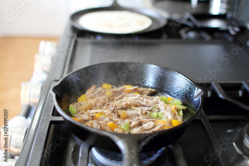 Mexican style pulled pork, known as carnitas, cooking in a cast iron skillet with a flour tortilla on a camal skillet.