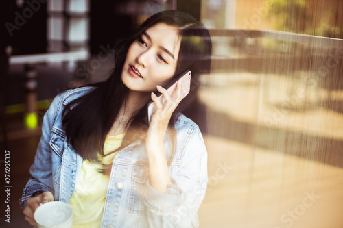 Asian woman with beautiful smile hold mobile phone during rest in coffee shop.Attractive woman drinking coffee.Reflection glass window.
