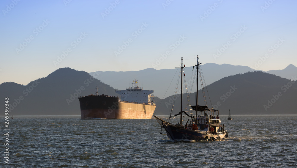 Obraz premium Schooner full of tourists strolling and a tanker in the background