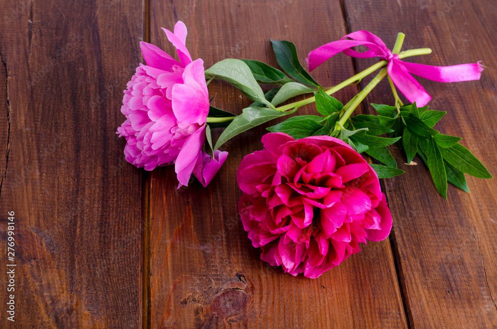 Two beautiful peonies with ribbon on wooden table