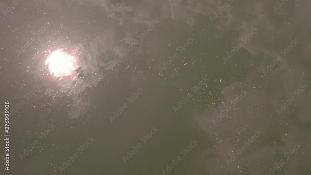 Low flight over lake surface, reflection of clouds in the greenish water surface. 4K