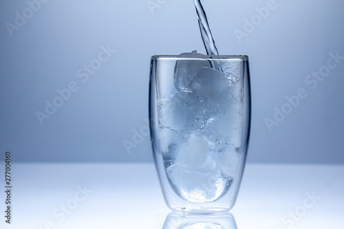 Pouring water into glass on blue background close up