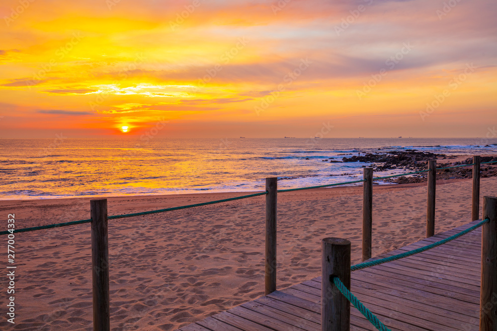 Sunset over the ocean. Wooden terrace on the sandy beach at sunset. Beautiful seashore in the evening. Porto, Portugal, Europe Sunset over the ocean. Wooden terrace on the sandy beach at sunset. Beautiful seashore in the evening. Porto, Portugal, Europe