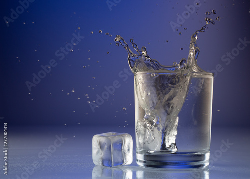 Pouring water into glass on blue background close up