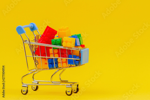 Shopping trolley cart full of colorful bricks on yellow background
