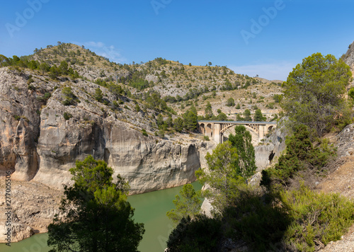 A beautiful historic arch bridge at the large reservoir Fuensanta in the Spanish region of Kastilla La Mancha. The water is turquoise green and the sun is shining.