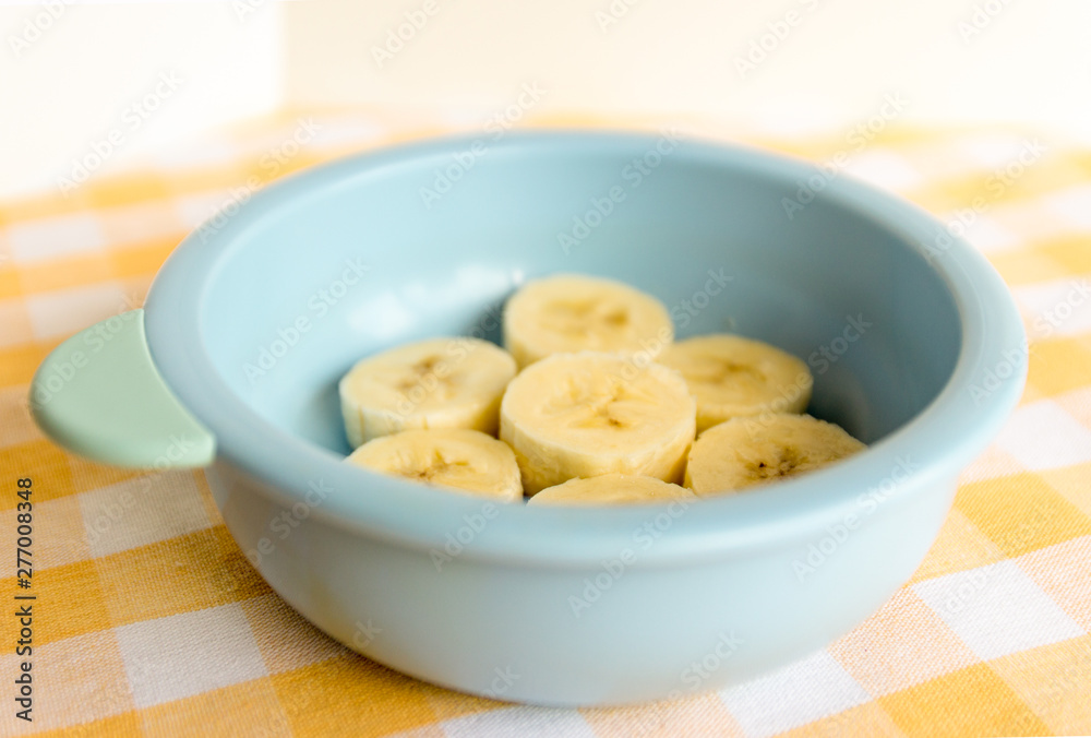 Preparing baby food, homemade.Top view of a bowl with cut banana in a blue bowl on a tablecloth. Healthy food kids concept. Selective focus.