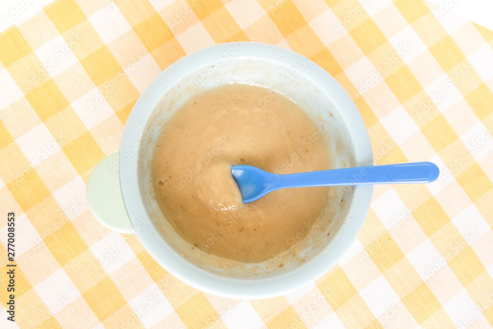 Preparing baby food, homemade.Top view of a bowl with smashed banana mixed with breast milk in a blue bowl on a tablecloth. Healthy food kids concept. Selective focus. Preparing baby food, homemade.Top view of a bowl with smashed banana mixed with breast milk in a blue bowl on a tablecloth. Healthy food kids concept. Selective focus.