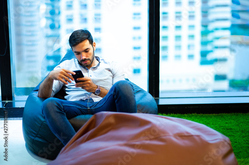 Young man sitting bean bag and use moile phone at modern office photo