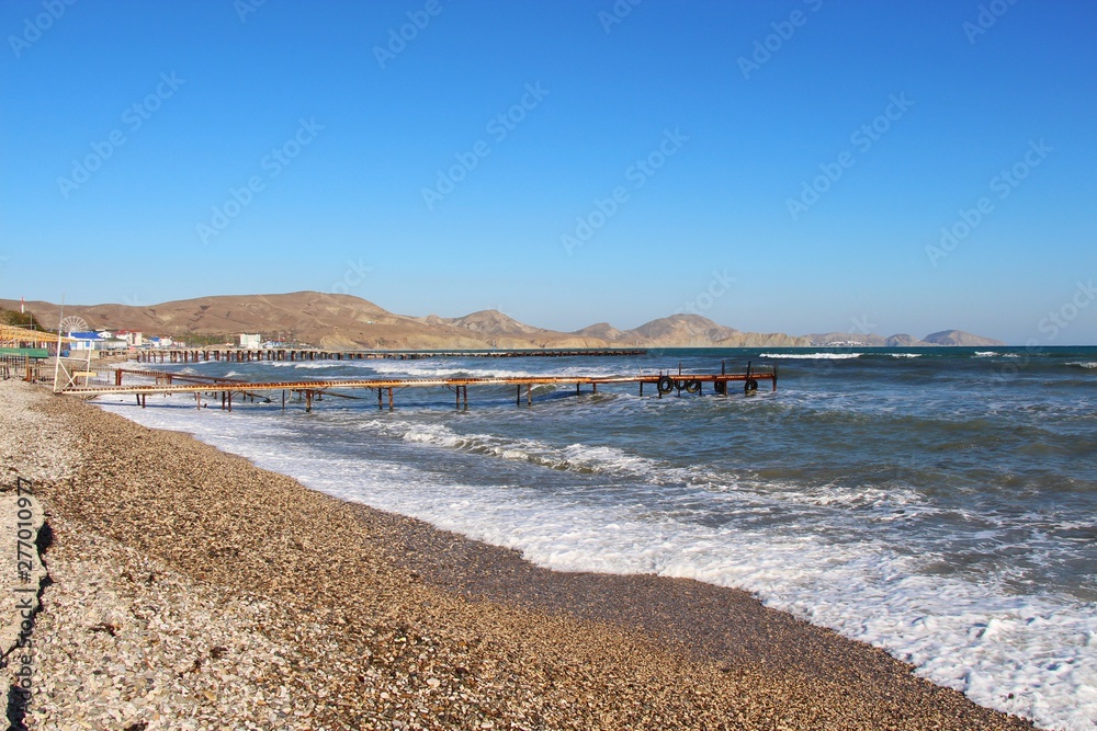 Empty pebble beach in Koktebel in the Crimea in mid-October. In the clear sunny weather, small waves runs onto the shore. Sea and ocean, nature, travel and tourism concept.