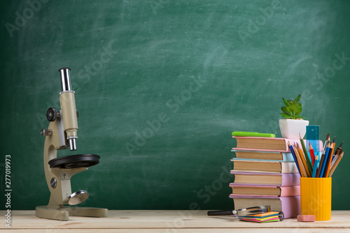 Education and science concept - group of colorful books and microscope on the wooden table in the classroom
