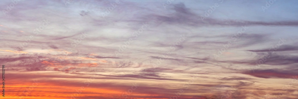 Orange and blue clouds on sunset lit sky, wide banner background that looks like painting