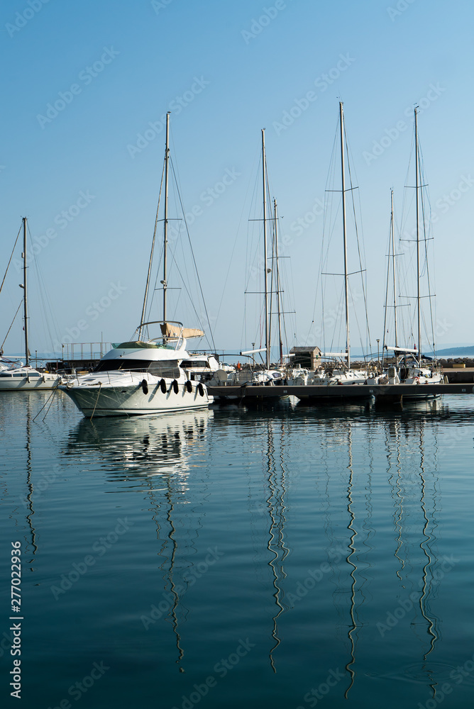 sailing yachts rest in bay on sunny day reflecting in water