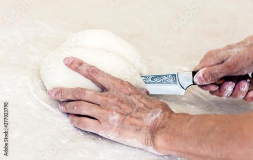 female hands with a knife cut the dough on the table in the kitchenю