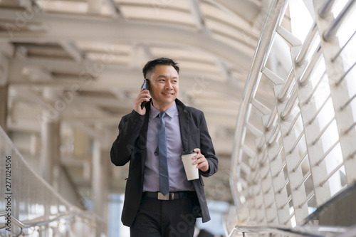 Asian Businessman walking and talking on mobile phone with business office buildings in the city background