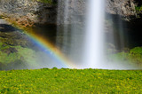 Scenic waterfall and rainbow background with green grass on the foreground