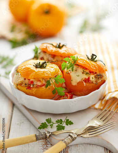 Stuffed tomatoes, baked yellow tomatoes stuffed with bulgur, vegetables and cheese with the addition of aromatic herbs in a baking dish on a white wooden table. Vegetarian food