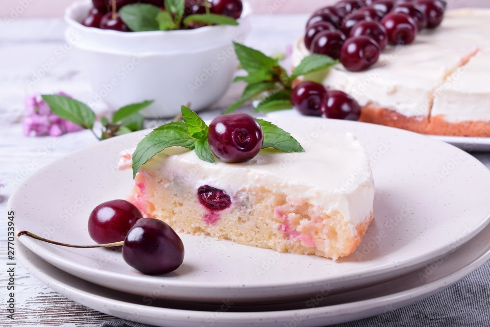 Piece of pie with sour cream and cherries topped with mint on the white plate