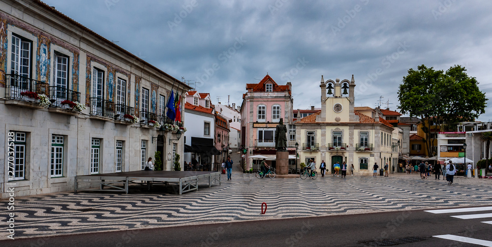 Central square in Cascais Portugal with the brightly painted buildings and a cloudy sky.