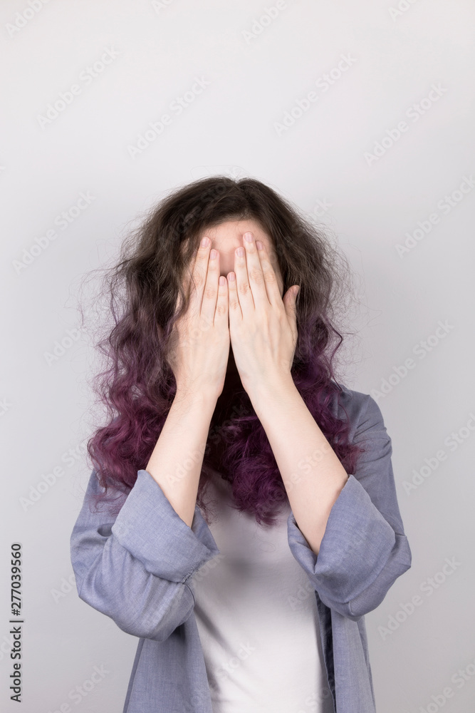 Young girl hides in palms face. Coloring purple hair. Gray background Young girl hides in palms face. Coloring purple hair. Gray background