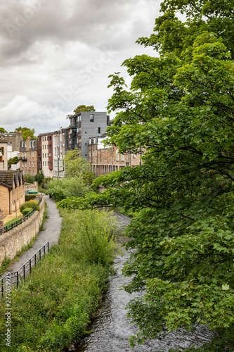 view down a bridge in Stockbridge, Edinburgh to the Water of Leith, with lush trees and a pathway