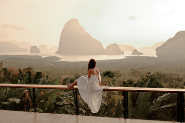 Woman with the white dress sit and see the mountain in early morning at the Sametnangshe Island viewpoint, Phang-Nga, Thailand.