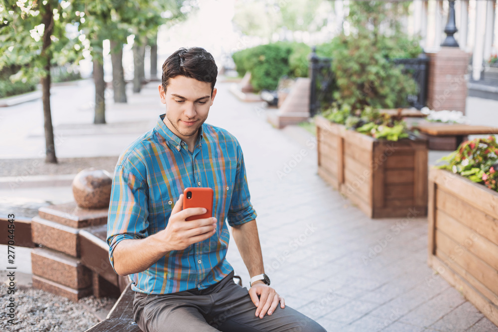 Obraz premium Young handsome business man using smartphone in a city. Cheerful men holding mobile phone. Travel, business, technology concept