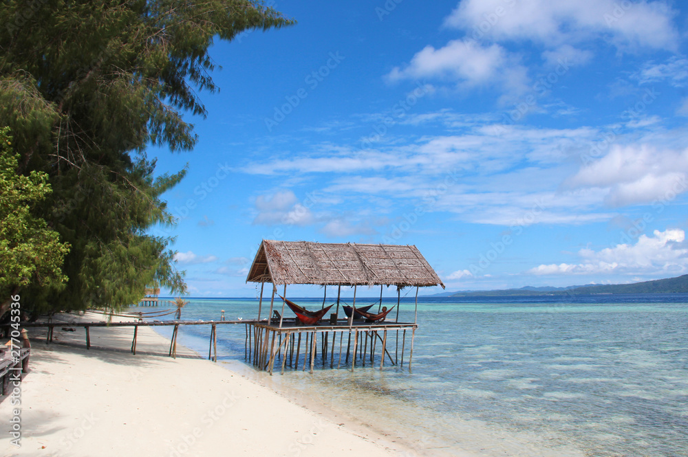Stilt platform with hammocks over the water on a tropical beach in Raja Ampat on a sunny day.