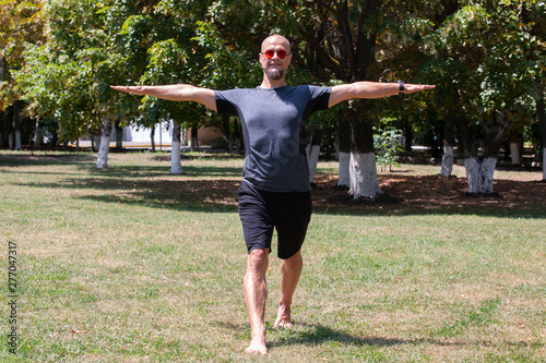 Young man training yoga outdoors. Sporty guy makes stretching exercise on a blue yoga mat, on the sports ground.