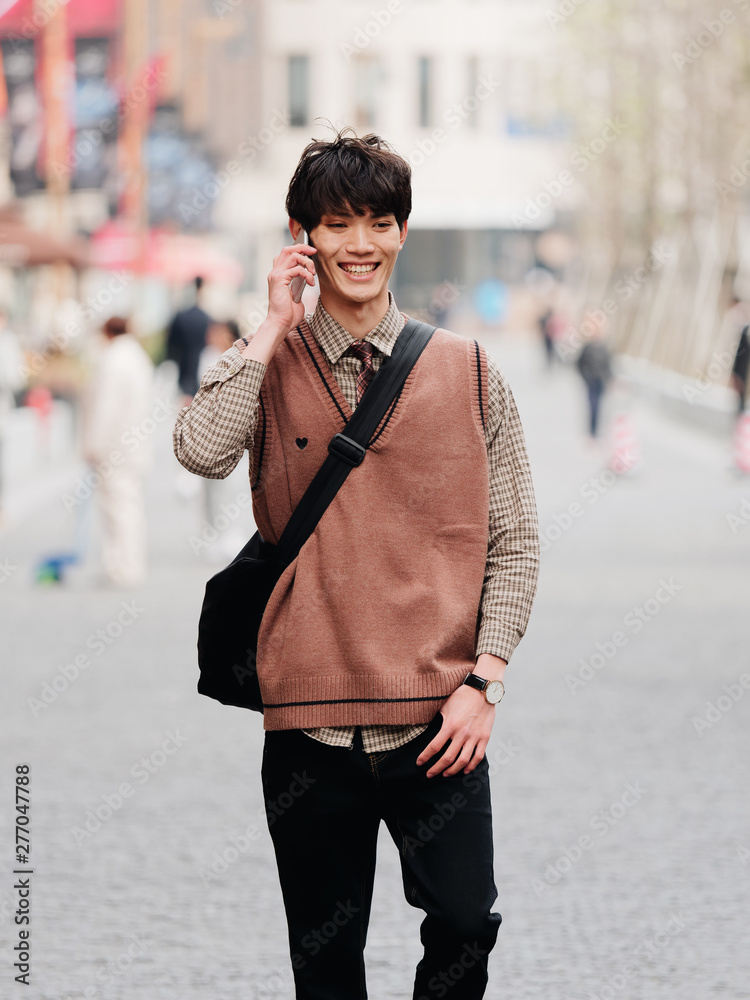 Portrait of a handsome Chinese young man with Korean style clothes walking  on street and talking in mobile phone with Shanghai Nanjing road  background, male fashion, cool Asian young man lifestyle. foto