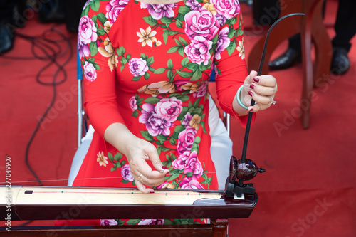 a woman dressed in traditional red with pink flower motif plays a ,Dan Bau (Đàn bầu) a vietnamese single stringed (monochord) instrument photo