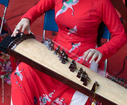 Photography a woman dressed in traditional red with bird motif plays a Dann Tranh (đàn thập