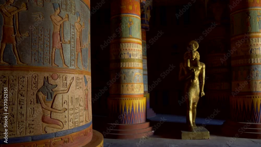 Interior of an Egyptian temple. Colorful columns covered with Ancient Egyptian characters and pictures of ancient people's life. Bronze colored statue of ram headed god Khnum (god of the source of the