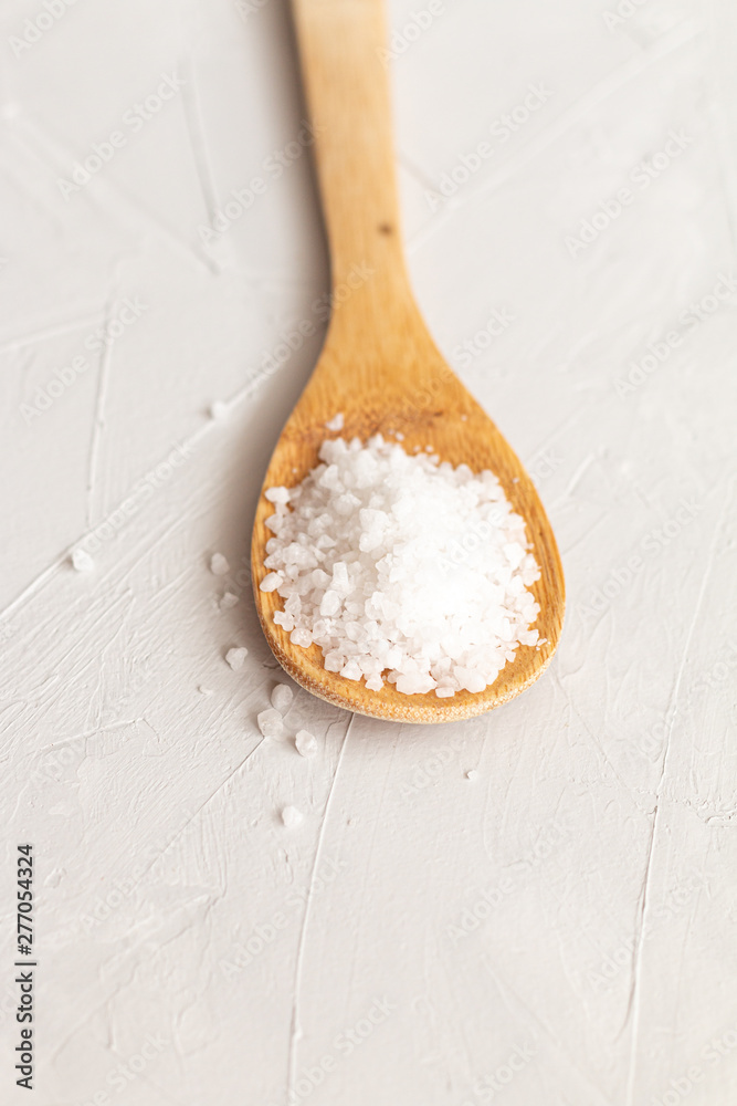 large sea salt in a wooden spoon on grey background. Food ingredients isolated
